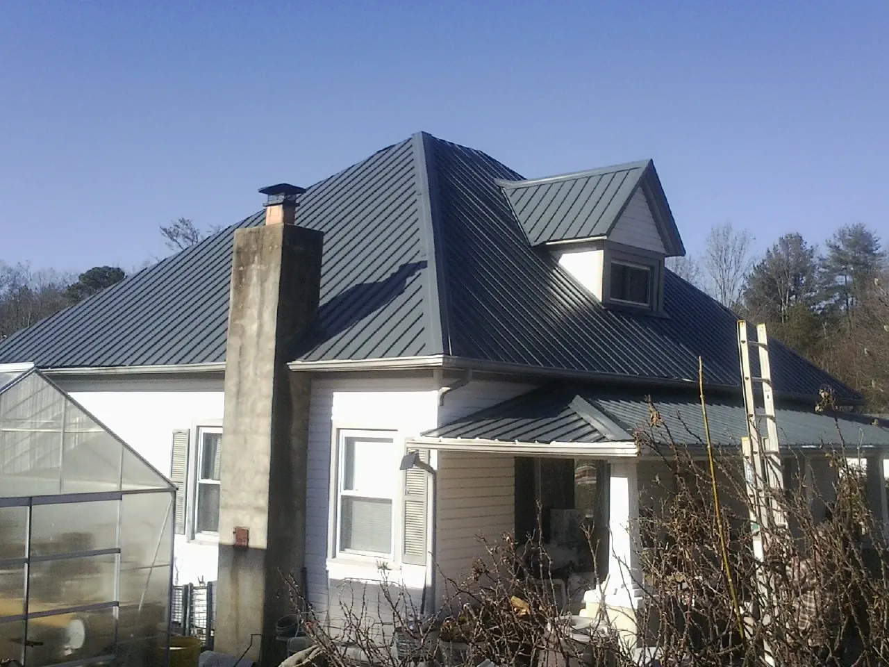 Dark blue standing seam metal roof on a white farmhouse with dormer — Slate & Tile Roof Repair by Roofing Brothers in Centerville